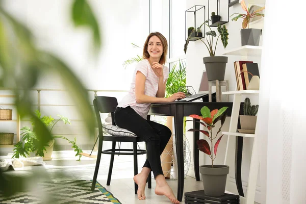 Giovane donna che usa il computer portatile a casa, spazio per il testo. Trendy interno camera con piante — Foto Stock
