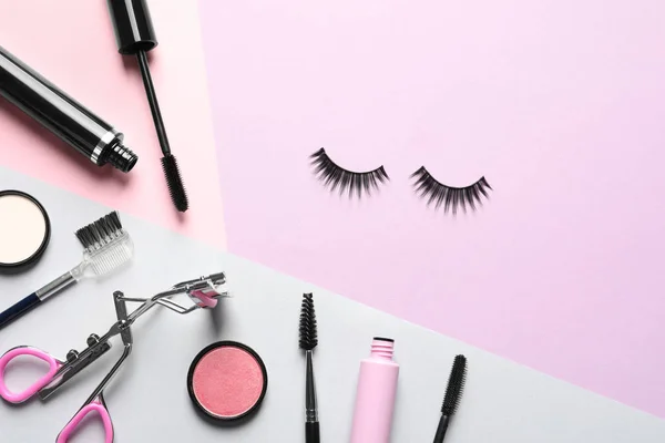 Flat lay composition with false eyelashes and other makeup products on color background, space for text