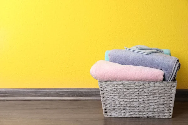 Basket with clean laundry on floor near yellow wall, space for text — Stock Photo, Image