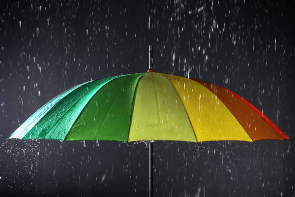 Bright umbrella under rain on dark background