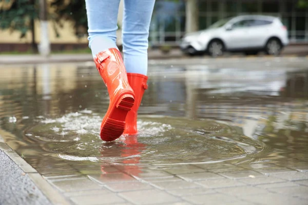 水たまりの中に赤いゴムのブーツを持つ女性、クローズアップ。雨天 — ストック写真