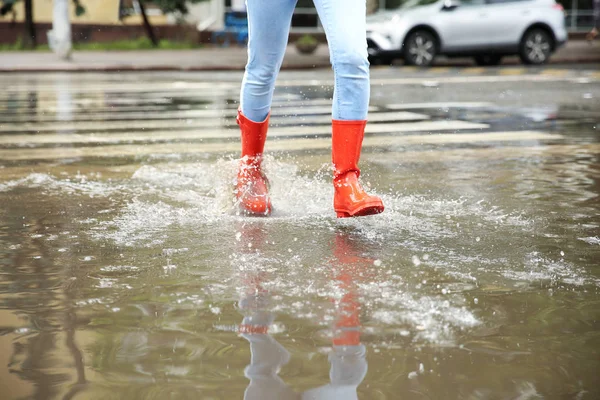 赤いゴムのブーツを持つ女性は、水たまりで実行され、クローズアップ。雨天 — ストック写真