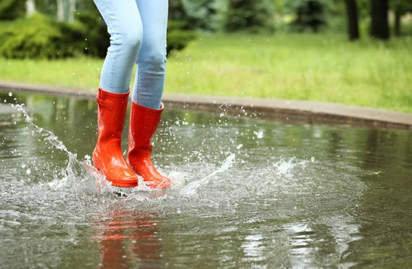 Жінка з червоними гумовими черевиками стрибає в калюжу, крупним планом. Дощова погода — стокове фото