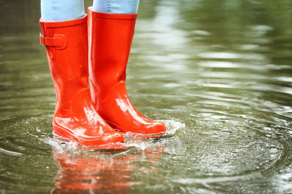 Woman with red rubber boots in puddle, closeup. Rainy weather