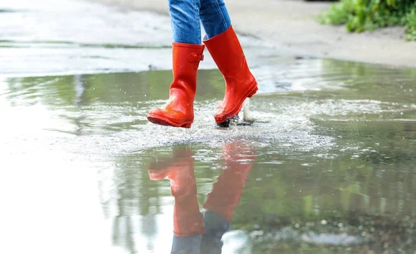 赤いゴムのブーツを持つ女性は、水たまりで実行され、クローズアップ。雨天 — ストック写真