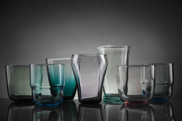 Set aus verschiedenen bunten leeren Gläsern auf dem Tisch vor grauem Hintergrund — Stockfoto
