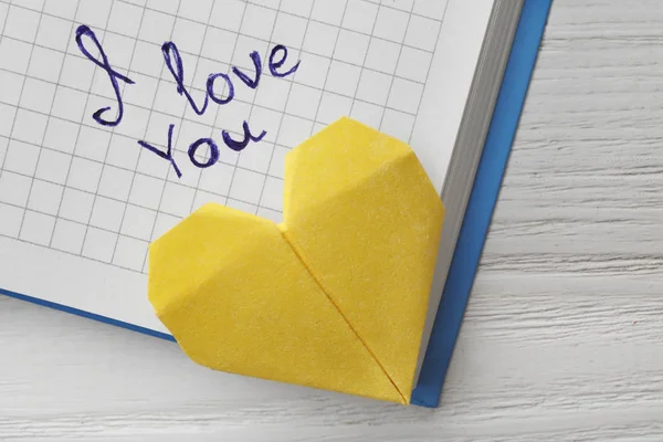 Notatnik z napisami i love you i serce origami na białym drewnianym stole, widok z góry — Zdjęcie stockowe