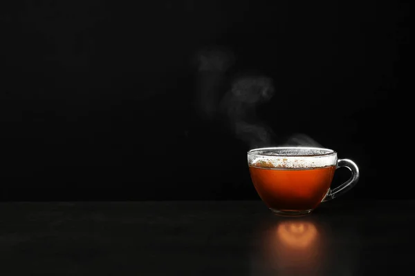 Copo de vidro de chá quente na mesa contra fundo preto, espaço para texto — Fotografia de Stock