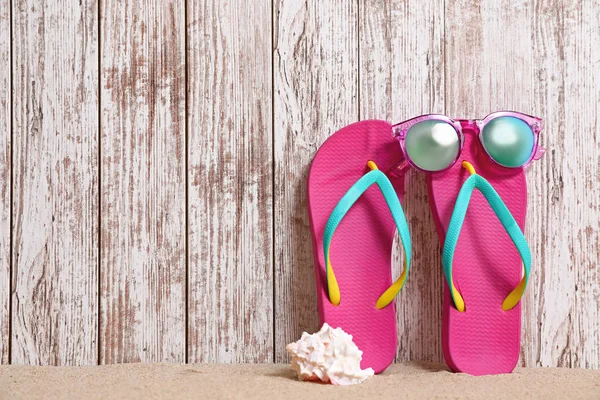 Infradito e occhiali da sole luminosi sulla sabbia vicino alla parete di legno, spazio per il testo. Accessori spiaggia estate — Foto Stock