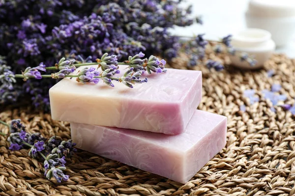 Handmade soap bars with lavender flowers on wicker mat, closeup