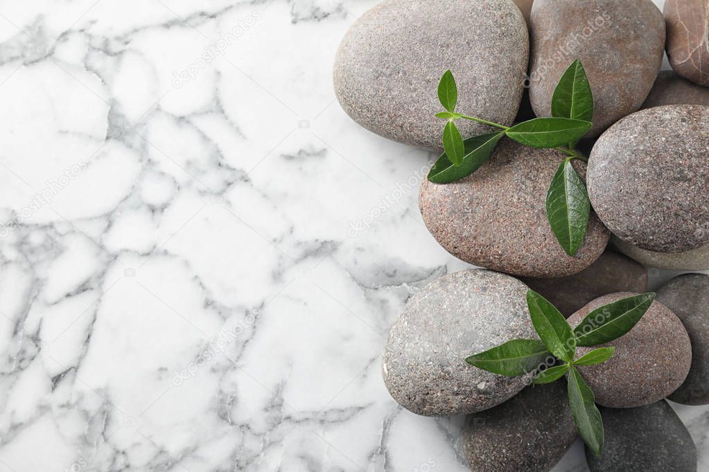 Spa stones and green leaves on marble table, flat lay with space for text