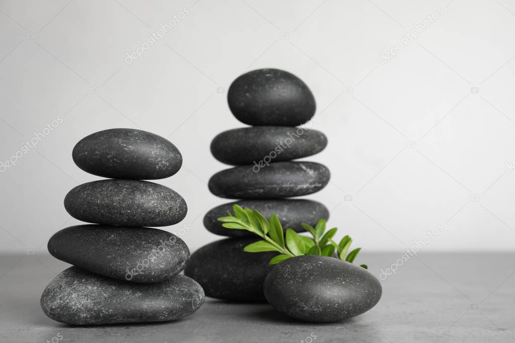 Stacks of spa stones and green leaves on grey table, space for text