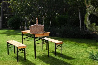 Yeşil parkta ahşap masa üzerinde piknik sepeti. Metin için alan