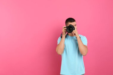 Genç profesyonel fotoğrafçı pembe arka planda fotoğraf çekiyor. Metin için alan