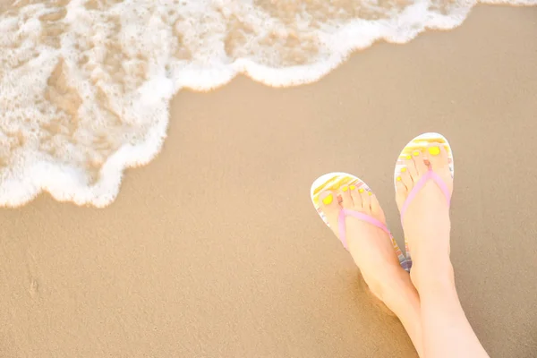 Closeup of woman with stylish flip flops on sand near sea, space for text. Beach accessories — Stock Photo, Image
