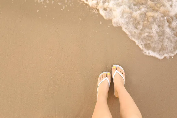 Bovenaanzicht van de vrouw met witte flip flops op zand in de buurt van zee, ruimte voor tekst. Strand accessoires — Stockfoto