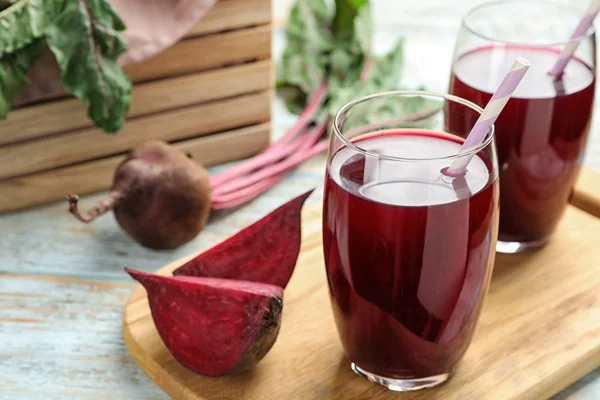 Tabla de madera con remolacha cortada y vasos de jugo en la mesa. Espacio para texto — Foto de Stock