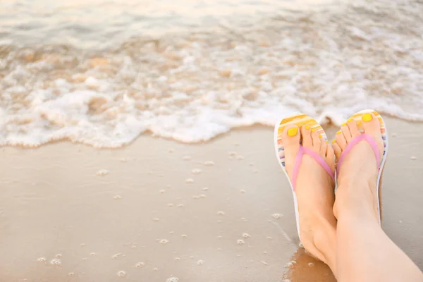 Close-up de mulher com chinelos elegantes na areia perto do mar, espaço para texto. Acessórios de praia — Fotografia de Stock