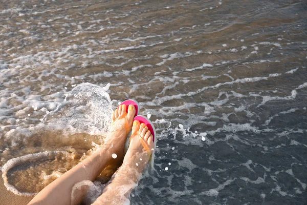 Gros plan de la femme avec des tongs sur le sable près de la mer, espace pour le texte. Accessoires de plage — Photo