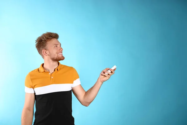 Young man with air conditioner remote on blue background. Space for text