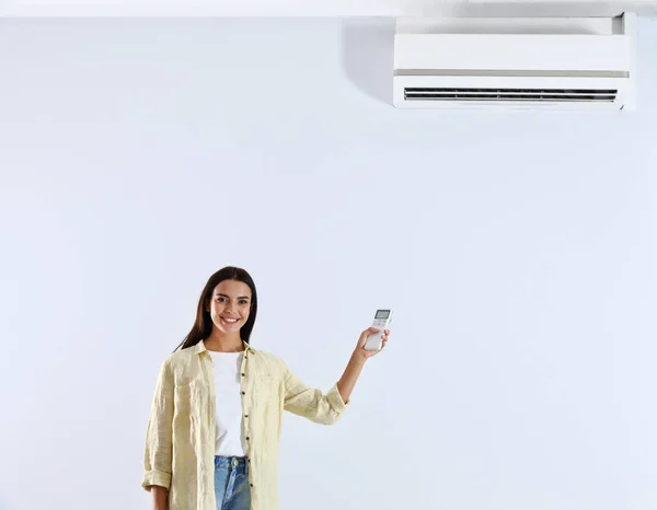 Junge Frau schaltet Klimaanlage vor weißem Hintergrund ein — Stockfoto