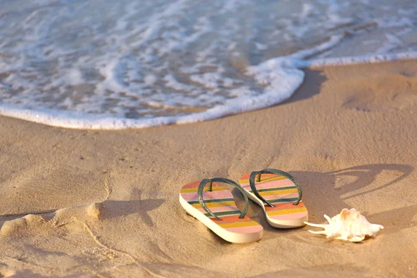 Chinelos elegantes e concha na areia perto do mar, espaço para texto. Acessórios de praia — Fotografia de Stock