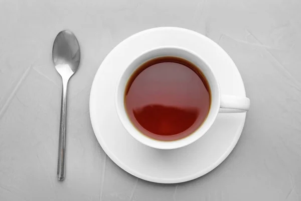 Tazza di tè con piattino e cucchiaio su sfondo grigio, posa piatta — Foto Stock