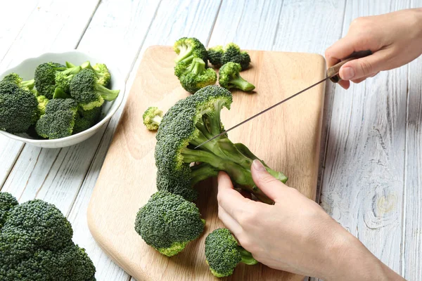 Kvinne som skjærer fersk grønn brokkoli med kniv på hvitt trebord, nærbilde – stockfoto