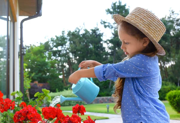 Kleines Mädchen, das rote Blumen im Hinterhof gießt. Gartenarbeit zu Hause — Stockfoto
