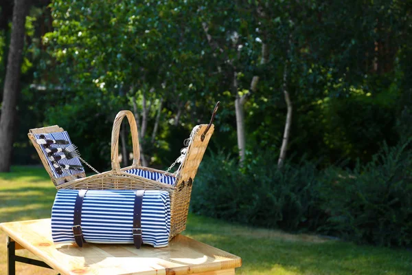 Offener Picknickkorb mit Decke auf Holztisch im grünen Park. Raum für Text — Stockfoto