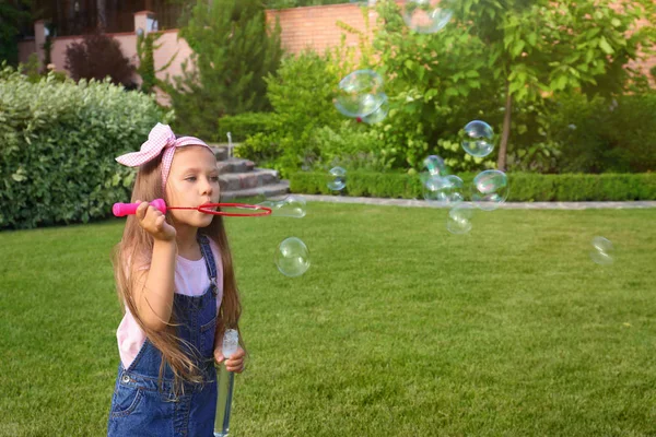 Linda niña soplando burbujas de jabón en el parque verde — Foto de Stock