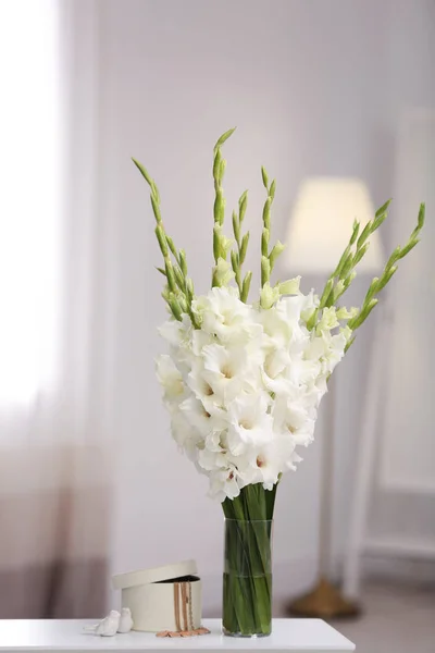 Florero con hermosas flores de gladiolo blanco y joyas en la mesa de madera en la habitación, espacio para el texto —  Fotos de Stock