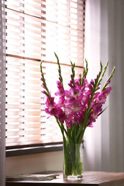 Jarrón con hermosas flores de gladiolo rosa en la mesa de madera en la habitación, espacio para el texto — Foto de Stock