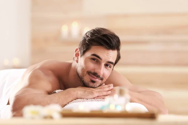 Joven guapo relajándose en la mesa de masaje en el salón de spa, espacio para el texto —  Fotos de Stock