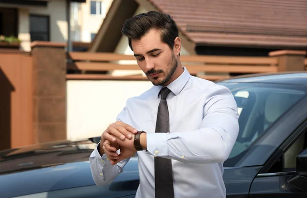 Attraente giovane uomo controllare il tempo vicino auto di lusso all'aperto — Foto Stock