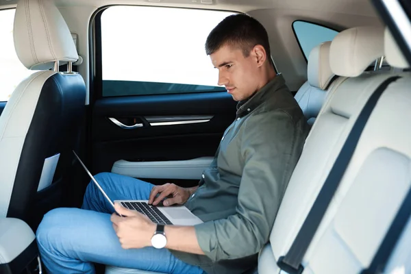 럭셔리 자동차의 뒷좌석에 노트북으로 작업 하는 매력적인 젊은 남자 — 스톡 사진