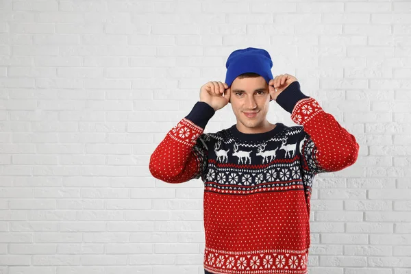 Portrait of young man in Christmas sweater and hat near white brick wall. Space for text — Stock Photo, Image