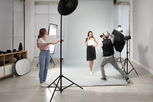 Fotógrafo profesional con asistente tomando fotos de una joven en un estudio moderno — Foto de Stock