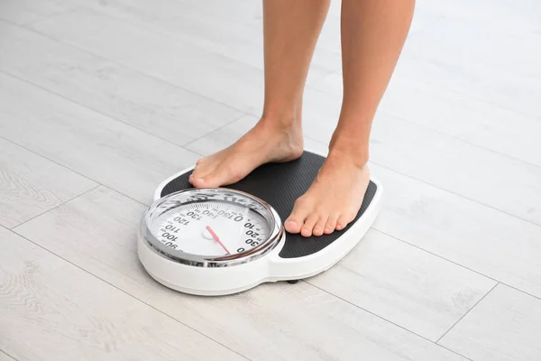 Kobieta stojąca na wadze w pomieszczeniu. Problem z nadwagą — Zdjęcie stockowe