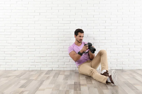 Ung fotograf med professionell kamera nära tegelvägg. Utrymme för text — Stockfoto