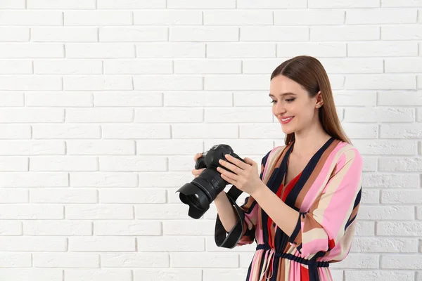 Fotógrafo profissional com câmera moderna perto da parede de tijolo branco. Espaço para texto — Fotografia de Stock