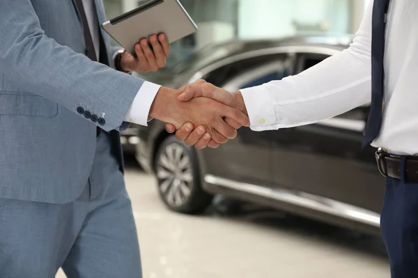 現代の自動車販売店でクライアントと握手する若いセールスマン、クローズアップ — ストック写真