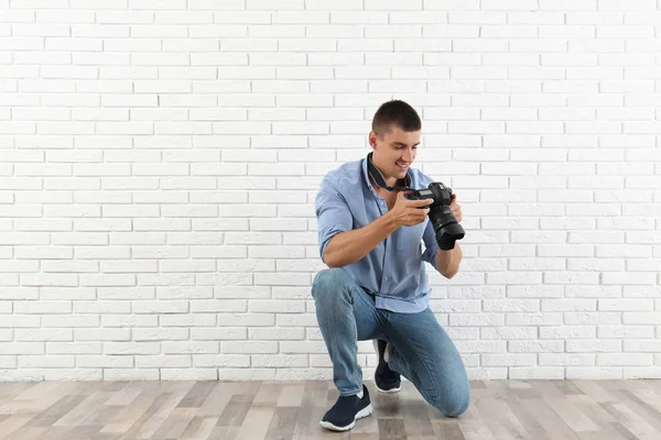 Ung fotograf med professionell kamera nära tegelvägg. Utrymme för text — Stockfoto