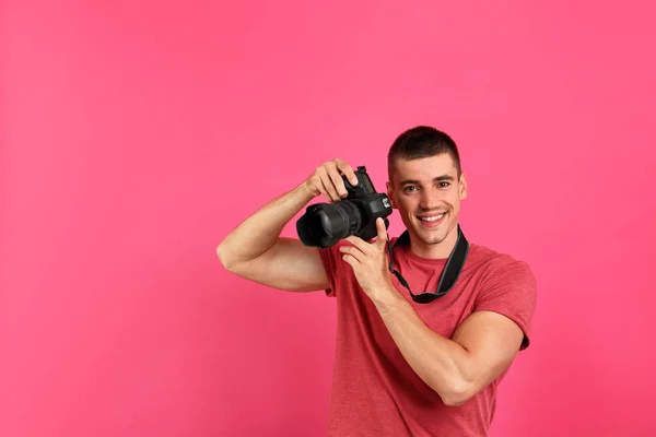 Joven fotógrafo con cámara profesional sobre fondo rosa —  Fotos de Stock