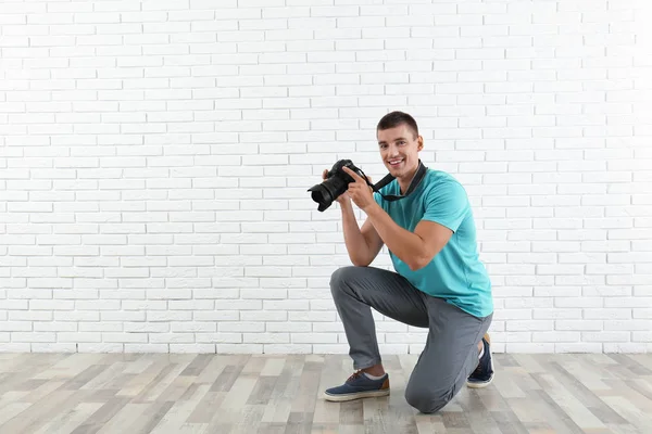 Jovem fotógrafo com câmera profissional perto da parede de tijolo. Espaço para texto — Fotografia de Stock