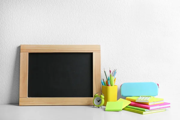 白い壁の近くの木製のテーブルの上に空白の小さな黒板と異なる学校の文房具。テキスト用のスペース — ストック写真