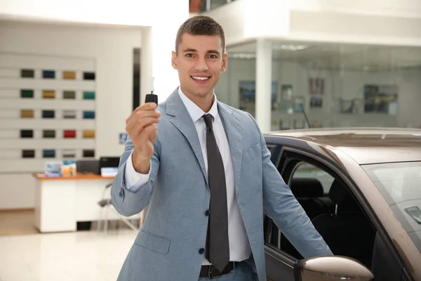 Jonge verkoper met sleutel in de buurt van auto in modern dealer — Stockfoto