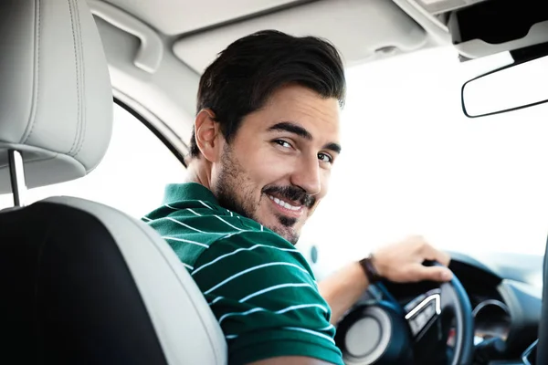 Atractivo joven conduciendo un coche de lujo, vista desde el asiento trasero — Foto de Stock