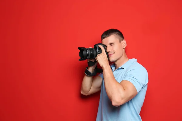 Jovem fotógrafo profissional tirando fotos em fundo vermelho. Espaço para texto — Fotografia de Stock