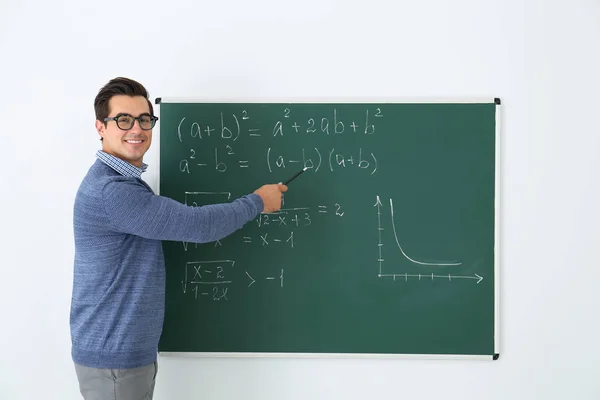 Giovane insegnante che spiega le formule matematiche scritte sulla lavagna in classe — Foto Stock